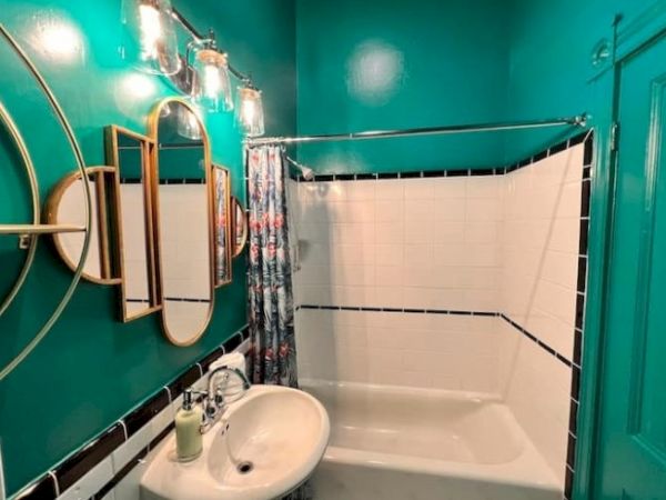 A vibrant bathroom features teal walls, a white sink, circular mirrors, and a bathtub with a tropical shower curtain.