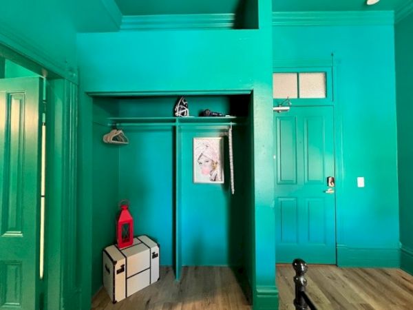 A teal room with an open closet, a red lantern, a decorative trunk, and a framed portrait on the wall.