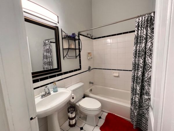 A small bathroom with a white sink, toilet, bathtub, and patterned shower curtain. Black and white tiles adorn the walls and floor.