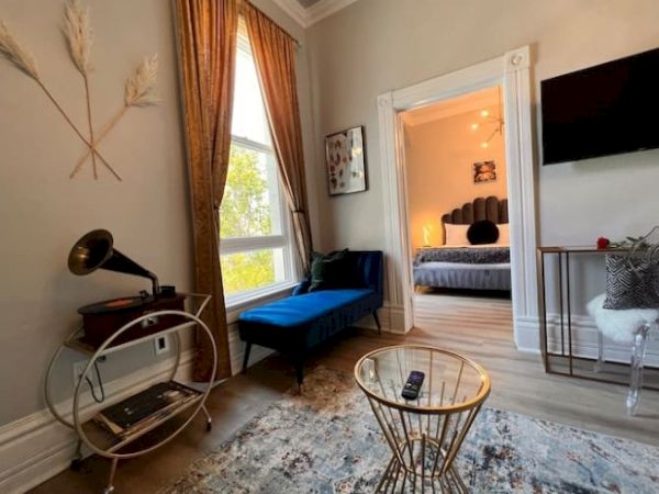 A stylish room with a gramophone, modern seating, TV, and view of a bedroom with a cozy bed, adorned with elegant decor and lighting.