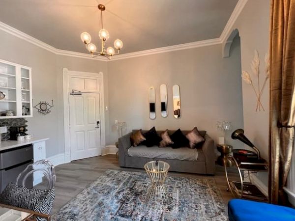 A cozy living room with a sofa, decorative pillows, a rug, wall art, and a chandelier. There are accents like mirrors and pampas grass.