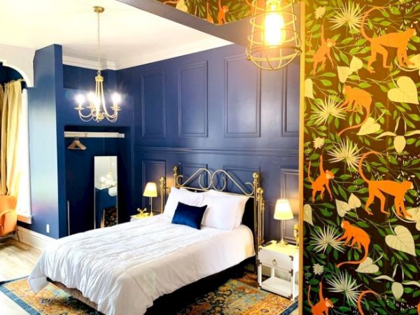 A vibrant bedroom features a blue accent wall, ornate metal bed, chandelier, and jungle-themed wallpaper with orange monkeys.