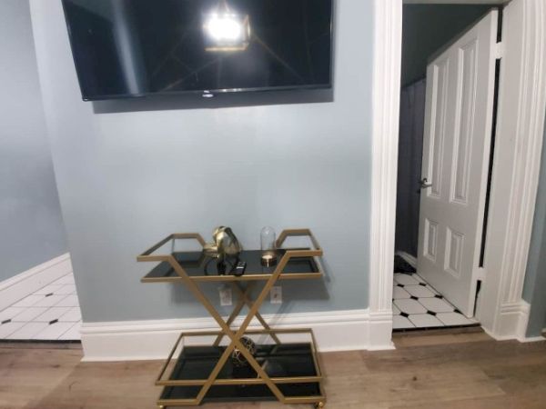 A hallway with a wall-mounted TV, a decorative cart with a gold frame, and a partially open door to a tiled room are visible.