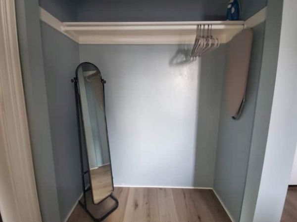 The image shows an empty closet with some hangers, a full-length mirror leaning against the wall, and an ironing board on the side.