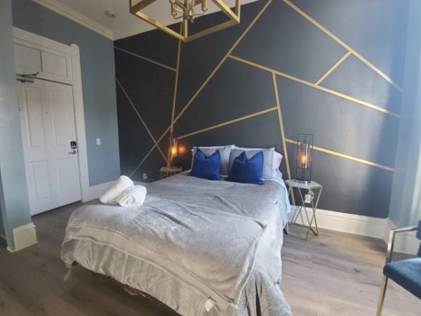 A modern bedroom with a geometric accent wall, bed with gray and blue linens, and a side table with candles, creates a cozy ambiance.