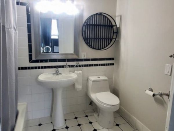 A bathroom with a pedestal sink, toilet, wall mirror, round shelf, tiled floor, and shower curtain. Modern and simple design.