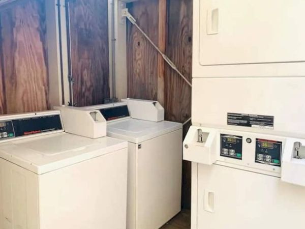 The image shows a laundry room with two washing machines and a stackable dryer set against wooden walls.