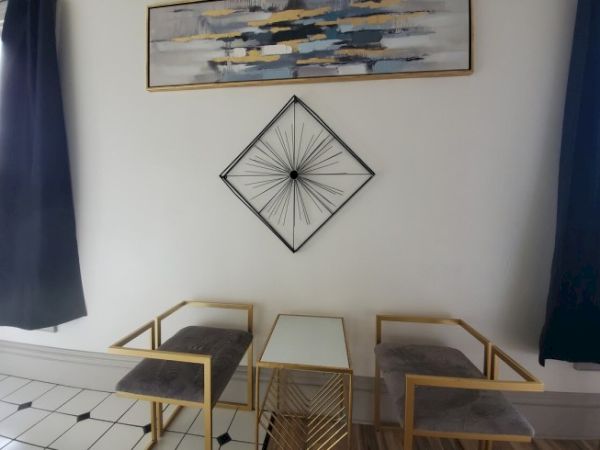 The image shows a modern setup with two chairs, a small table, abstract wall art, and geometric decor on a tiled floor.