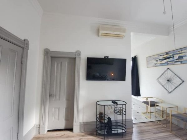A minimalist room with a mounted TV, decorative wire stand, modern art, gray doors, and an air conditioner. Bright walls create a cozy ambiance.