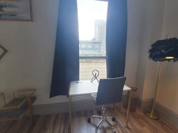 A small office setup with a desk, chair, and lamp by a window. A decorative item is on the desk, and cityscape is visible outside.
