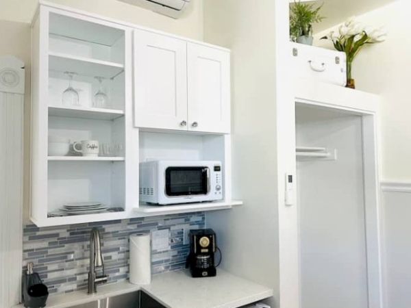 A compact kitchen with white cabinets, microwave, coffee maker, sink, backsplash, and decorative plants on top of a cabinet.