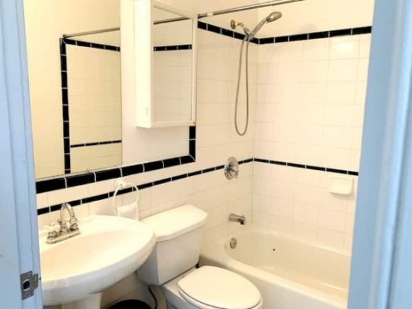 A small bathroom with white tiles, black accents, a bathtub, toilet, sink with mirror, and showerhead mounted above the bathtub.
