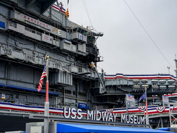 A close-up of the USS Midway Museum, featuring its signage, flags, and intricate ship details.