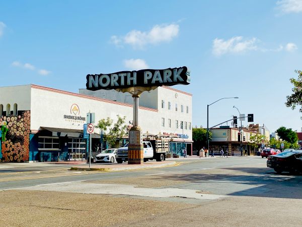 Street scene featuring a "North Park" sign, buildings, parked cars, and a clear sky.
