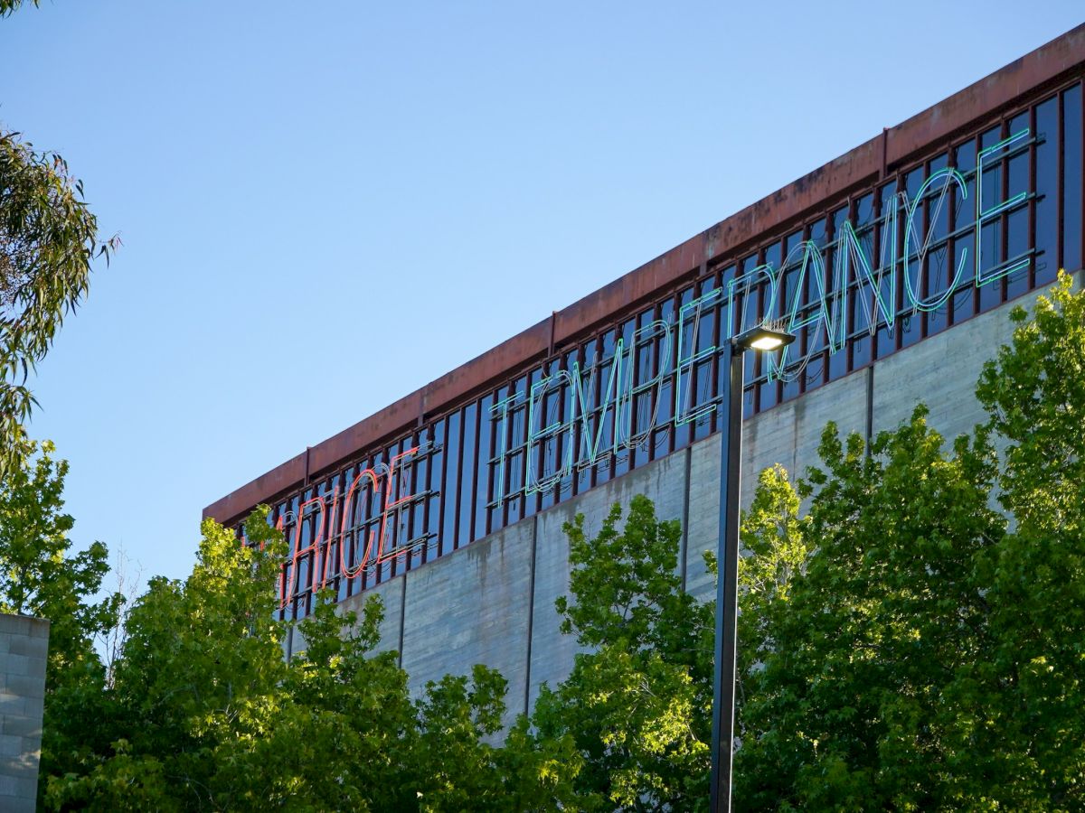 The image shows a building facade with the words "The Performance" partially visible, surrounded by trees and a clear blue sky.
