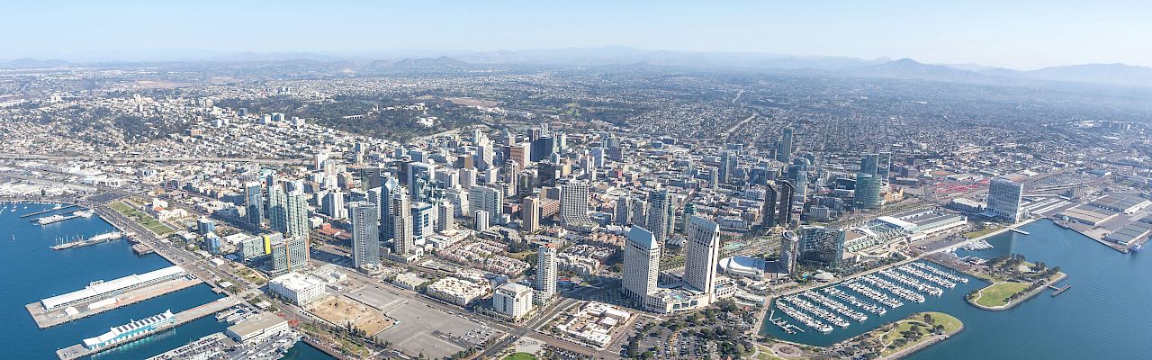 Aerial view of a coastal cityscape with skyscrapers, marinas, and a sprawling urban area by the water.