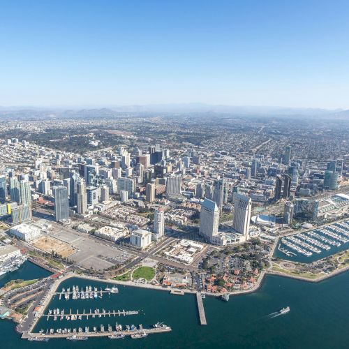 Aerial view of a coastal cityscape with skyscrapers, marinas, and a sprawling urban area by the water.
