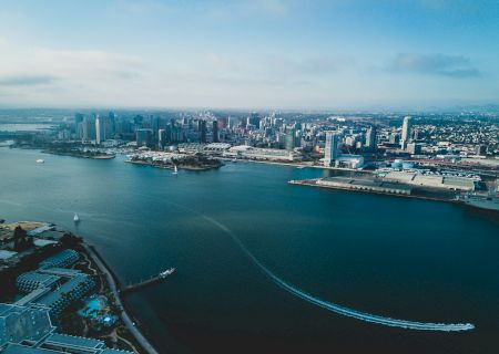 Aerial view of a coastal city with boats on the water, high-rise buildings, and clear skies in the distance.